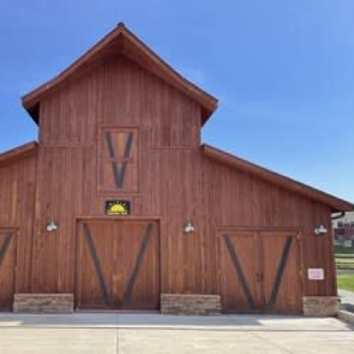 A large wooden barn with a pointed roof and two wide doors at the front, set against a clear blue sky.
