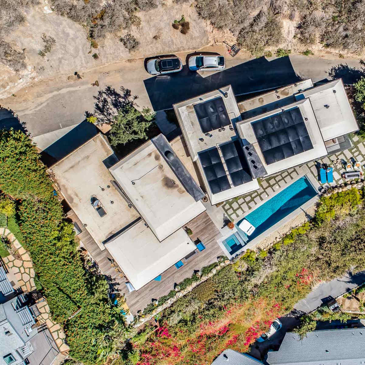 An aerial view of a residential property featuring multiple buildings, a swimming pool, and landscaped gardens along a winding road.