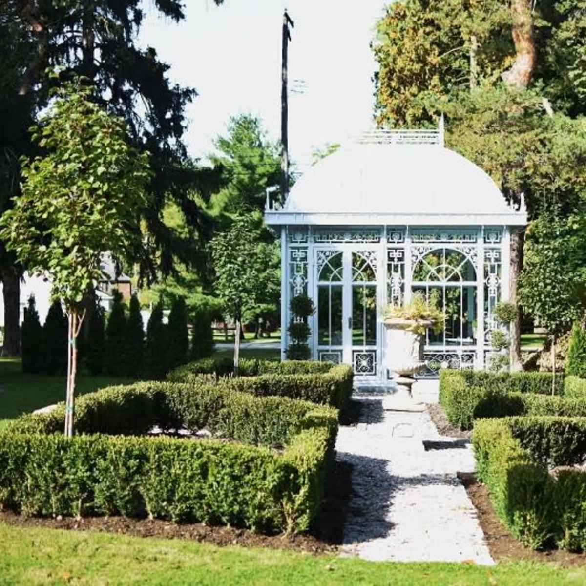 A decorative garden gazebo surrounded by neatly trimmed hedges and ornamental trees.