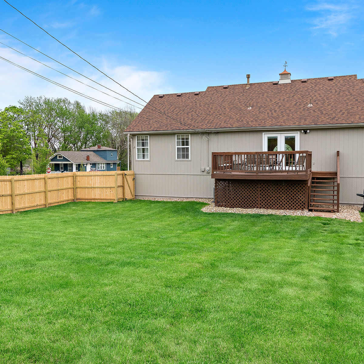 A fenced backyard with a well-manicured lawn and a two-story house featuring a deck and a barbecue grill.