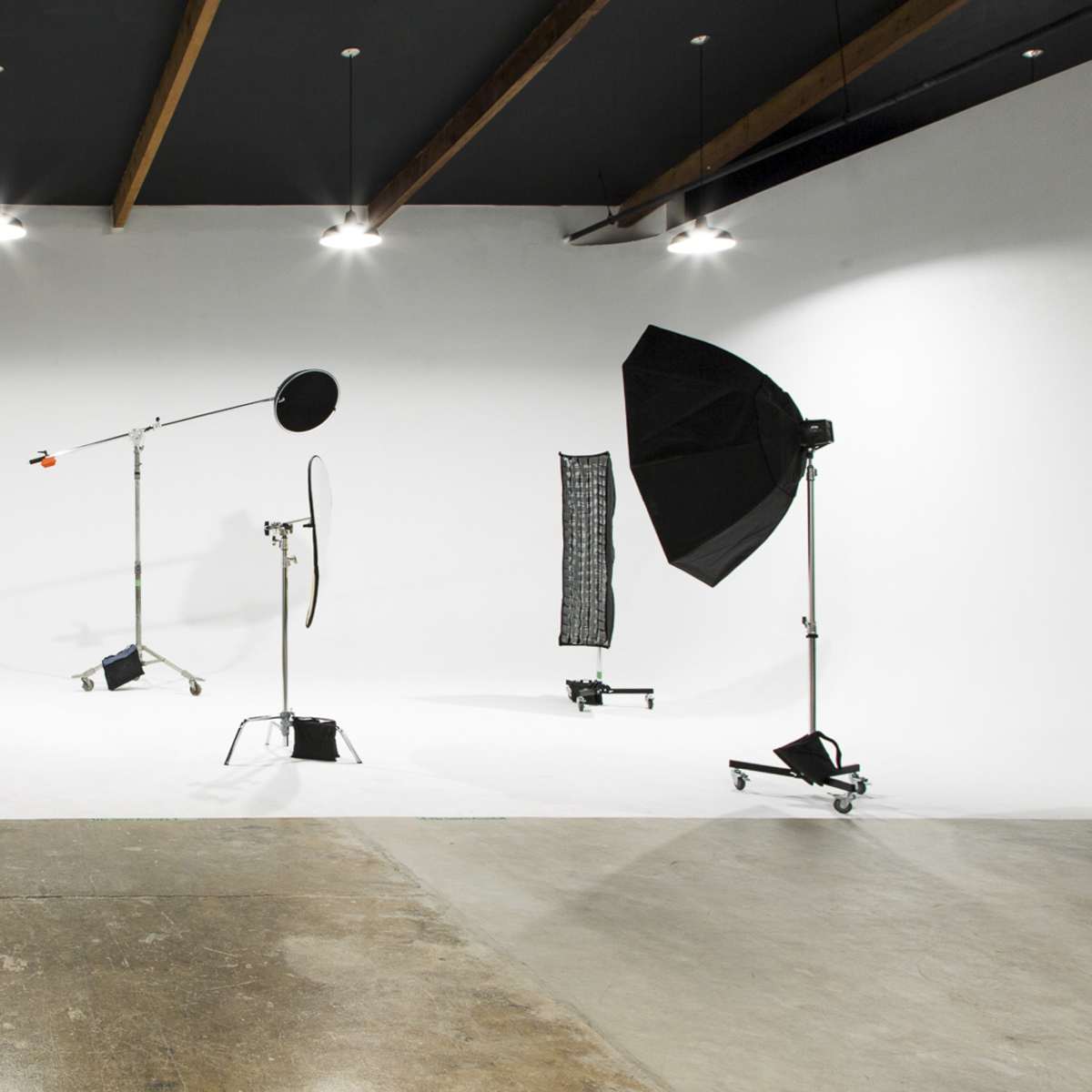 A photography studio with a white backdrop, lighting equipment, and a concrete floor.