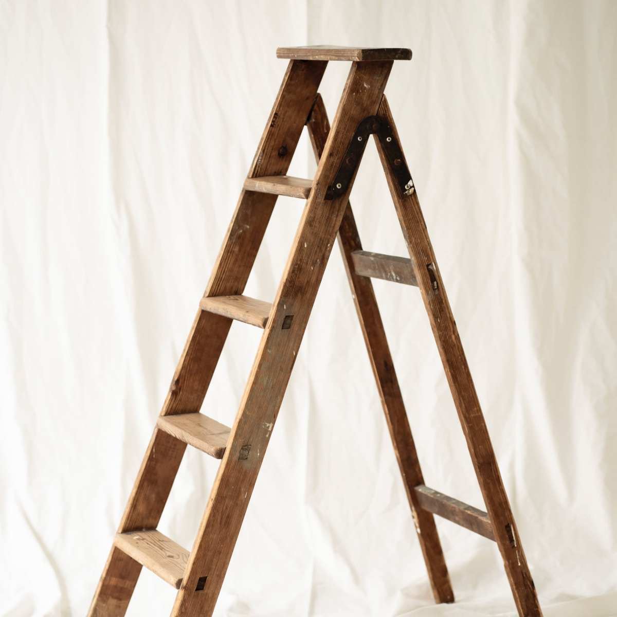 A wooden step ladder stands against a white backdrop.