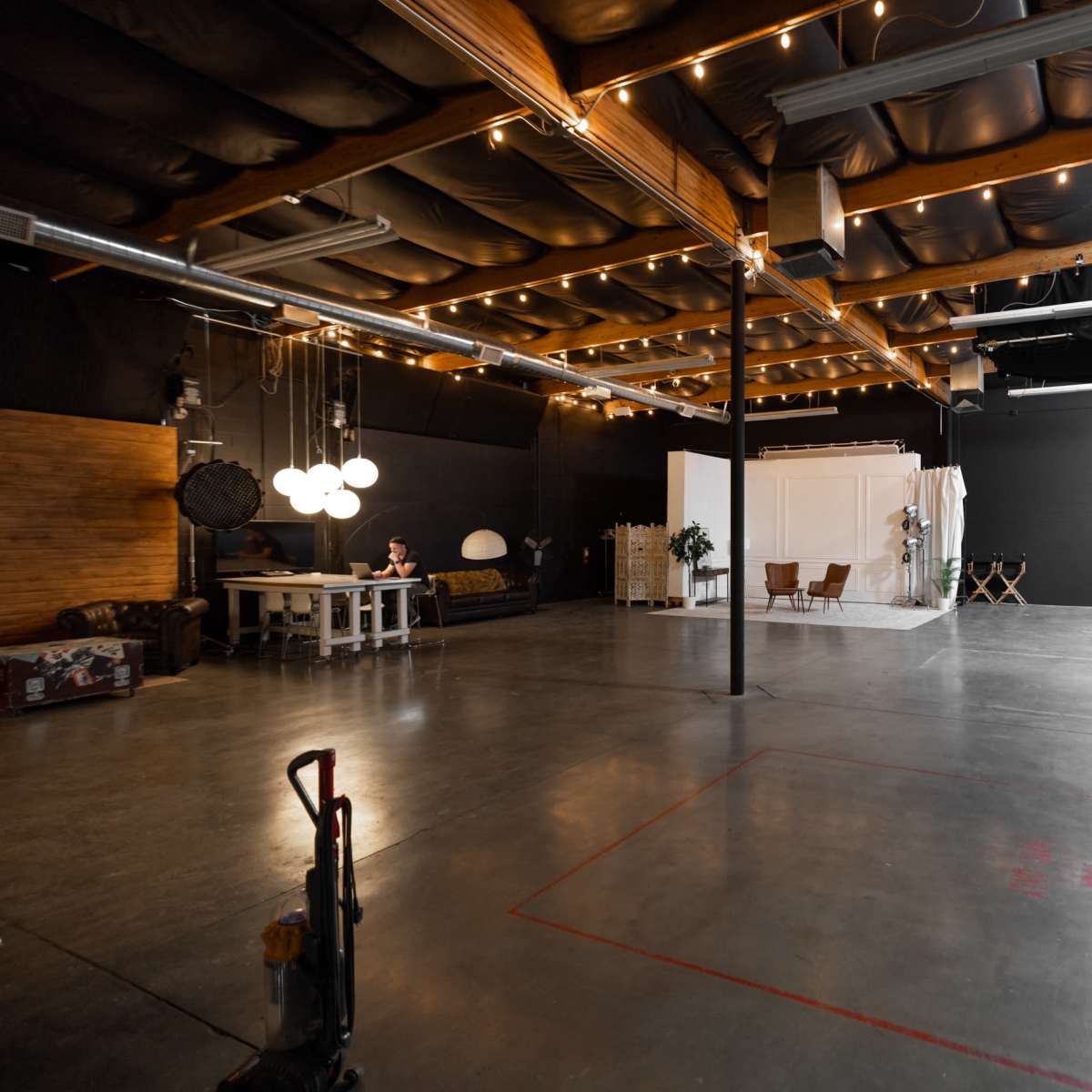 An expansive, industrial-style studio space with a polished concrete floor, wooden beams, and soft lighting.