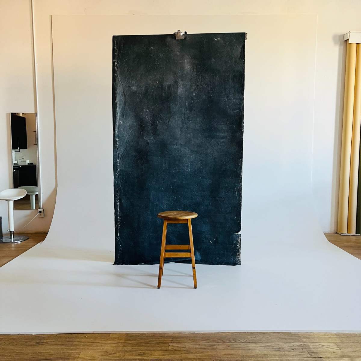 A wooden stool stands in front of a large, dark backdrop within a photo studio.