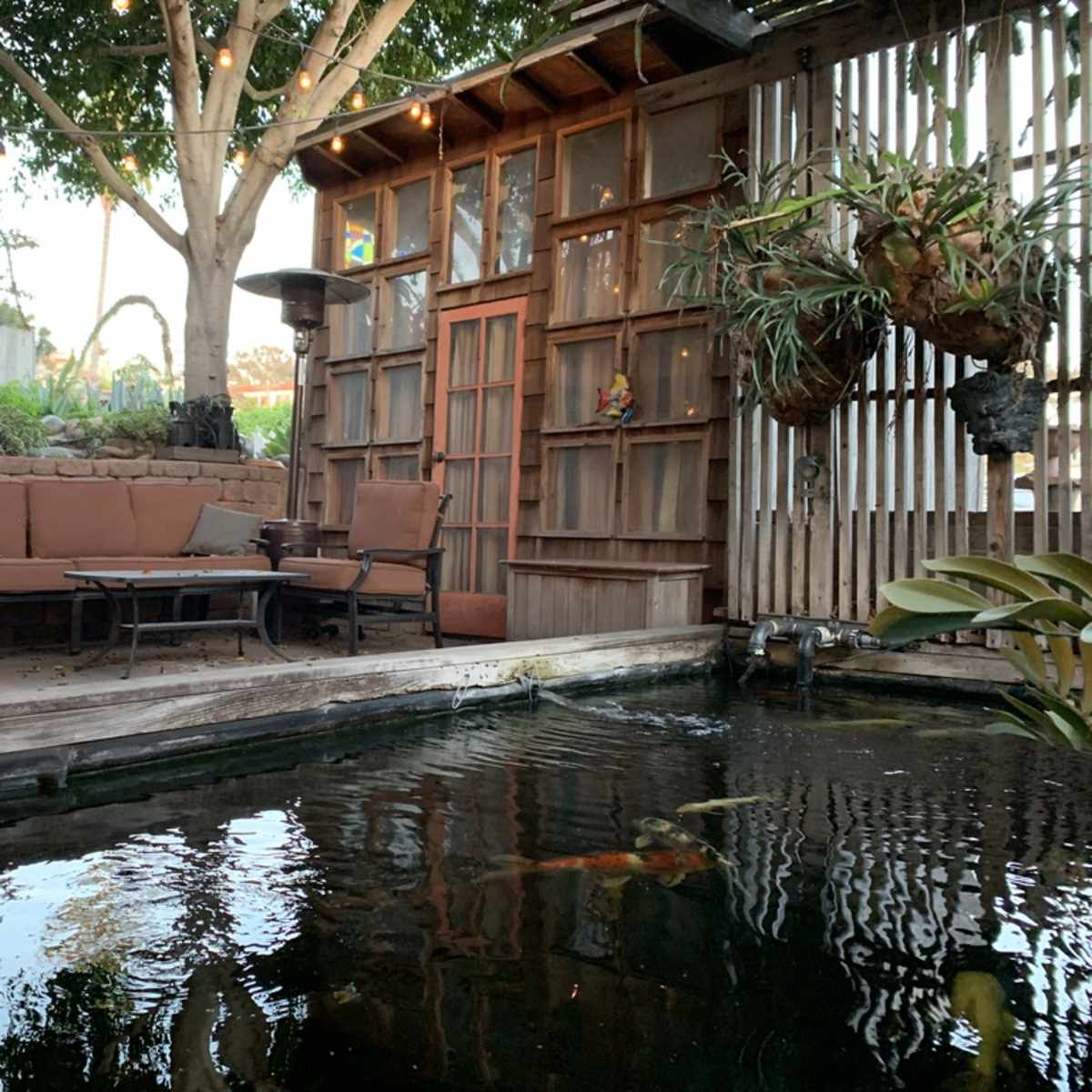 A cozy outdoor seating area beside a koi pond, surrounded by plants and wooden structures.