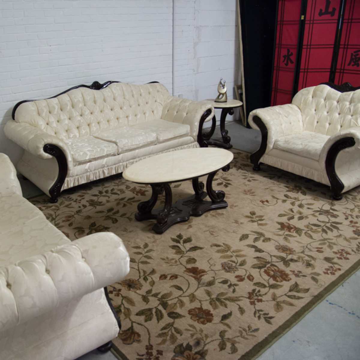 A furnished seating area featuring a white tufted sofa, two matching chairs, and a coffee table on a floral-patterned rug.