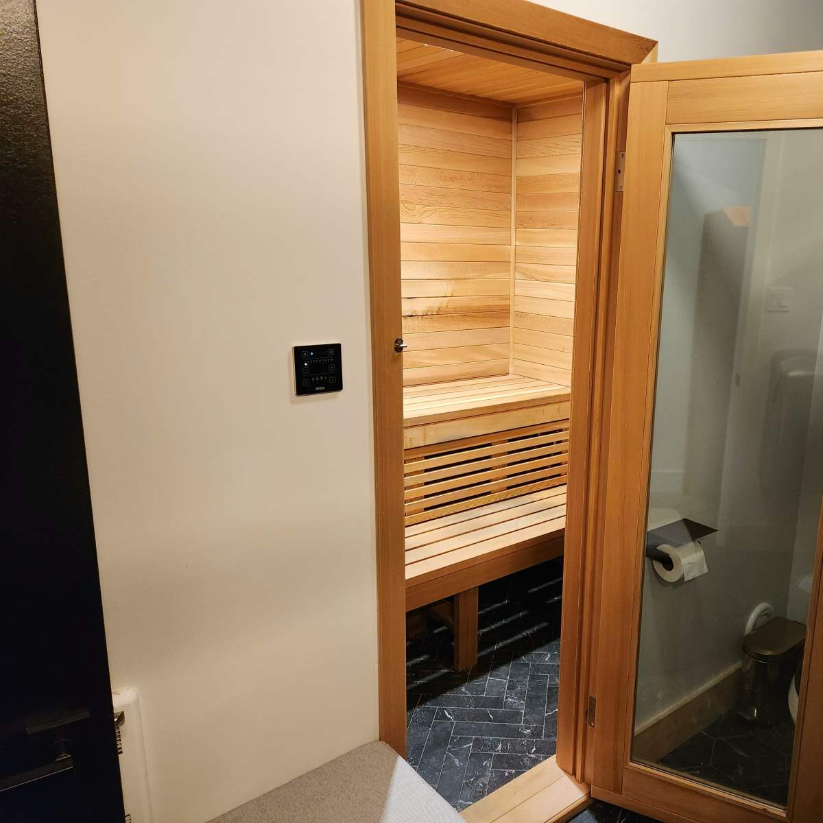 A bathroom featuring a wooden sauna with a glass door, adjacent to a toilet area.