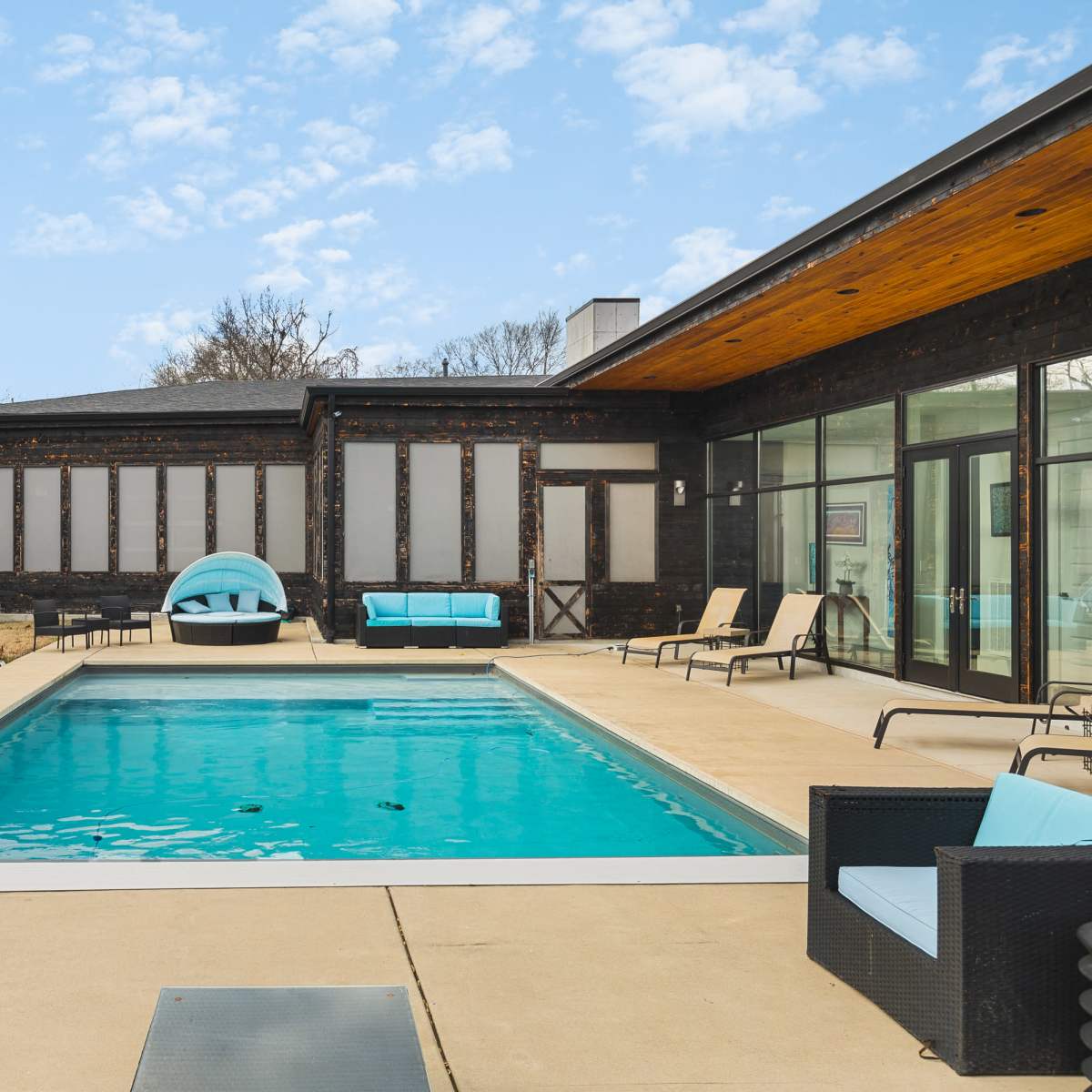 A swimming pool surrounded by lounge chairs and a house with a modern design.