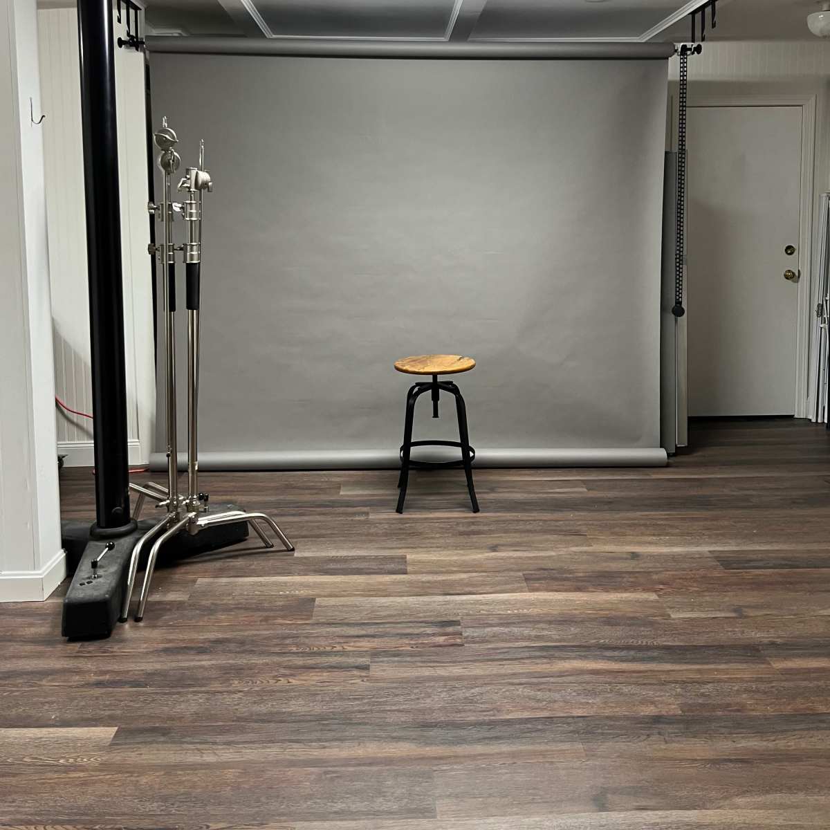 A photo studio with a gray backdrop, a wooden stool in the center, and studio lights on either side.