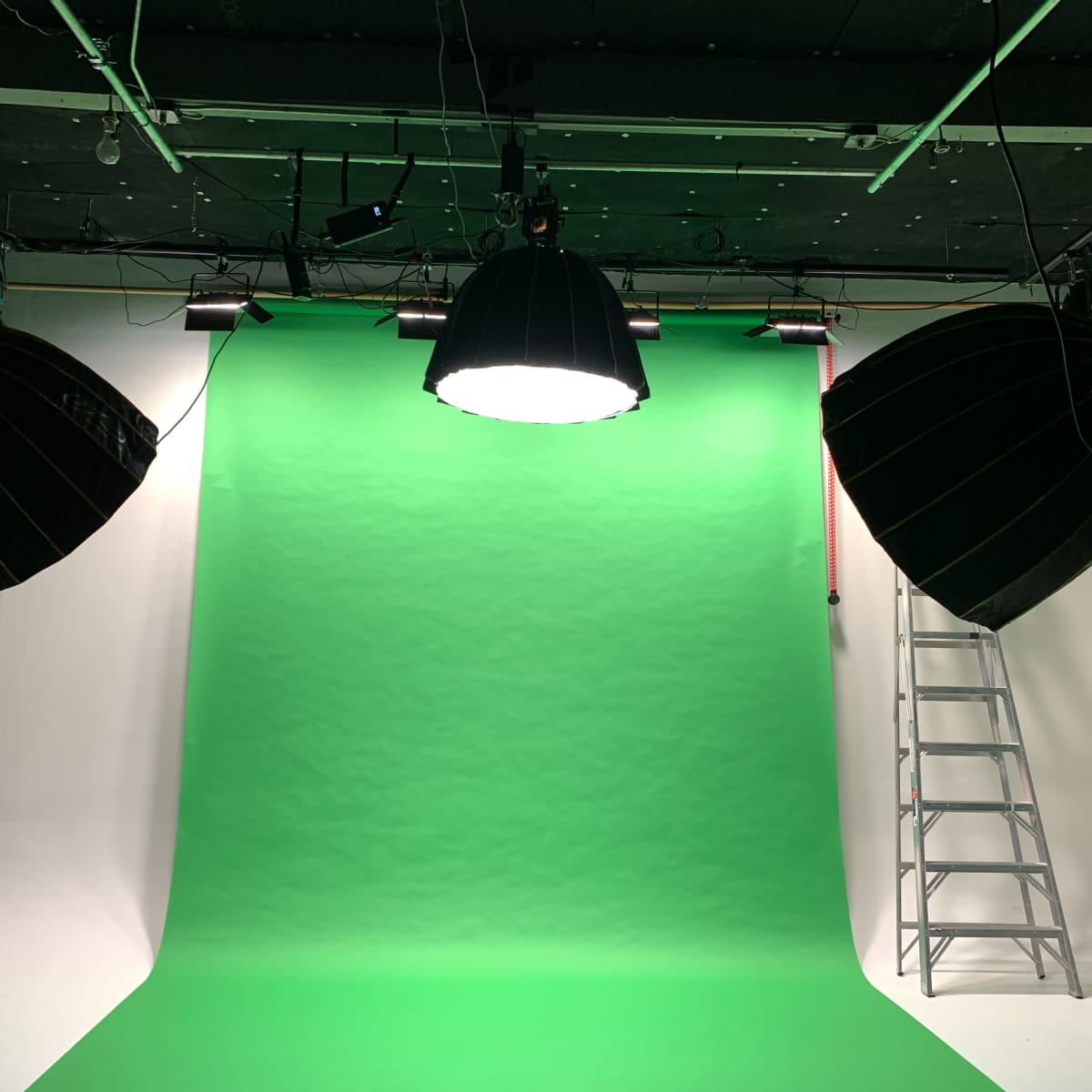 A photography studio with green screens, two large softbox lights, and a ladder in the background.