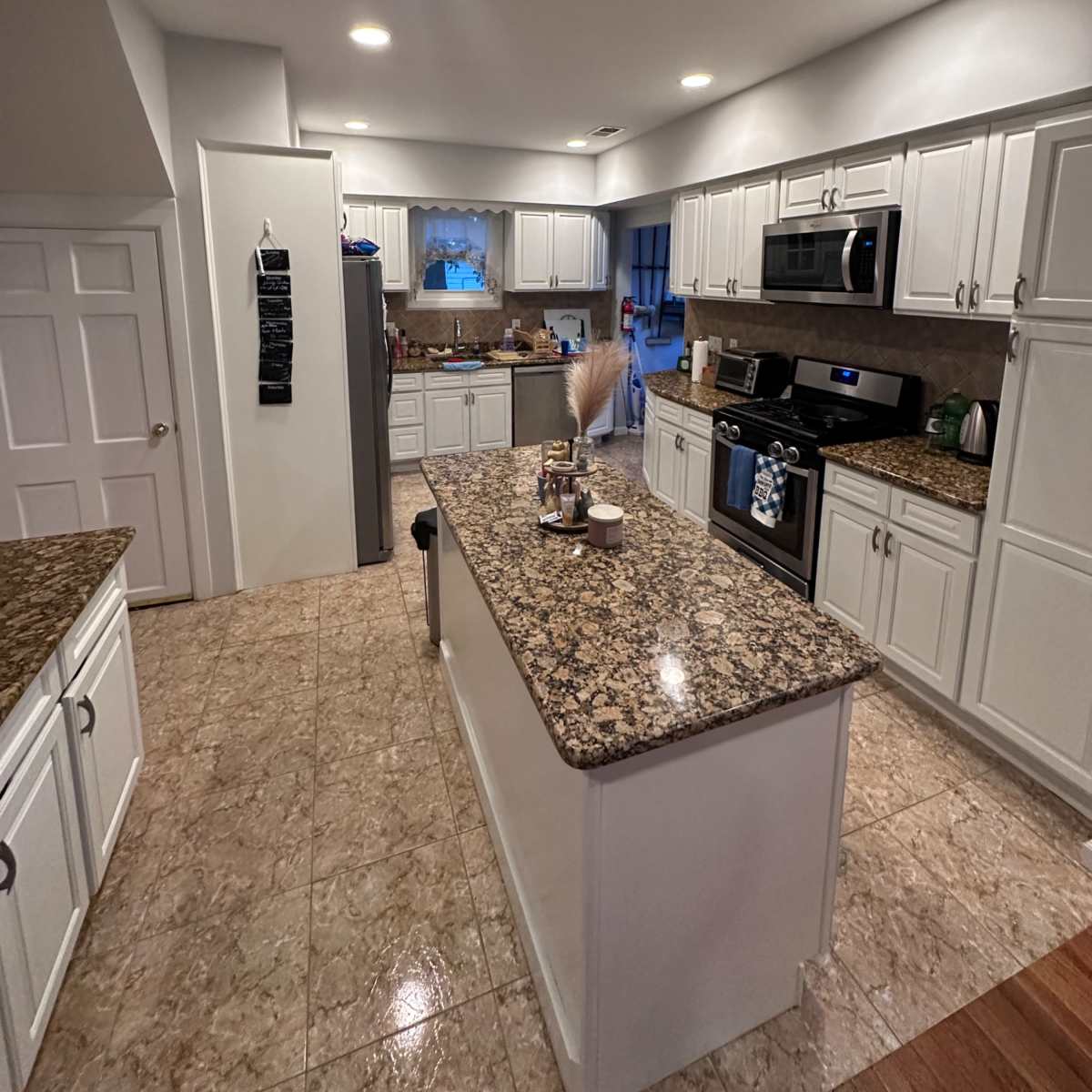 A modern kitchen with granite countertops, white cabinets, and stainless steel appliances, featuring an island in the center.