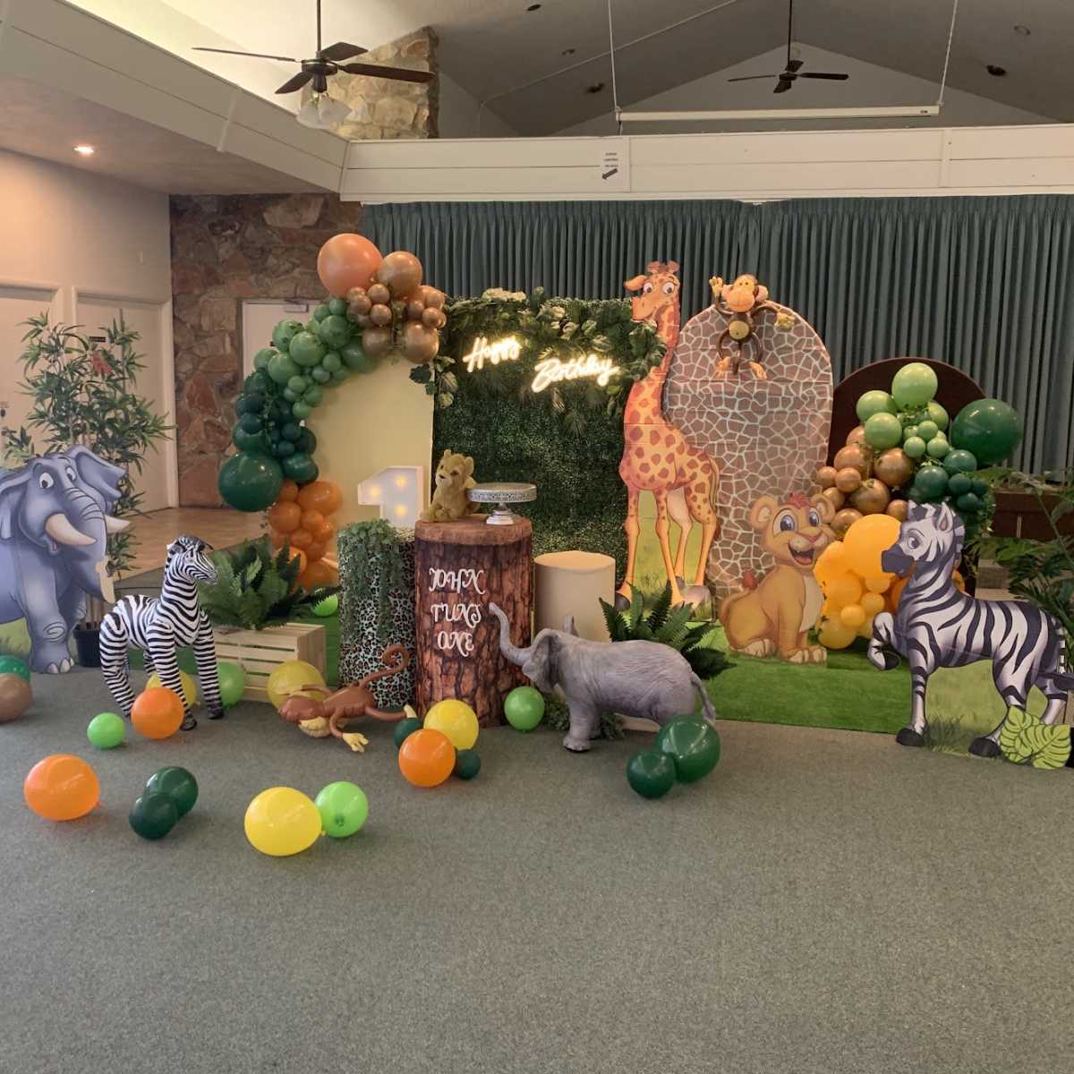 The scene features a vibrant jungle-themed decorations setup with animal cutouts, balloons, and a greenery backdrop for a celebration.
