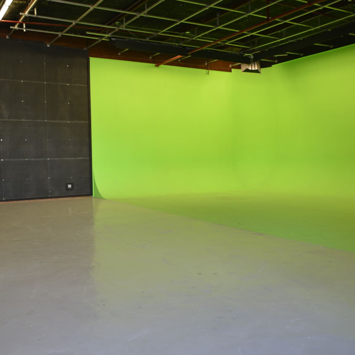 A spacious room featuring a black wall, a green backdrop, and a polished gray floor.