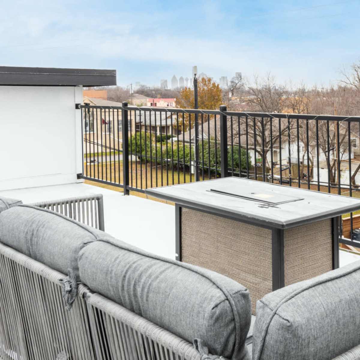 A rooftop patio with a seating area and a fire pit, overlooking a cityscape and residential backyards.