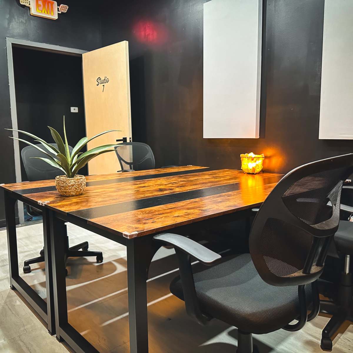 A small meeting room featuring a wooden table, four black office chairs, and a potted plant, with a door labeled "Studio 7" in the background.