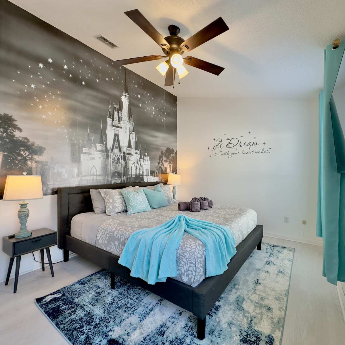 The room features a bed with a light blue throw blanket and a large mural of a castle on the wall, accompanied by two bedside lamps and curtains.