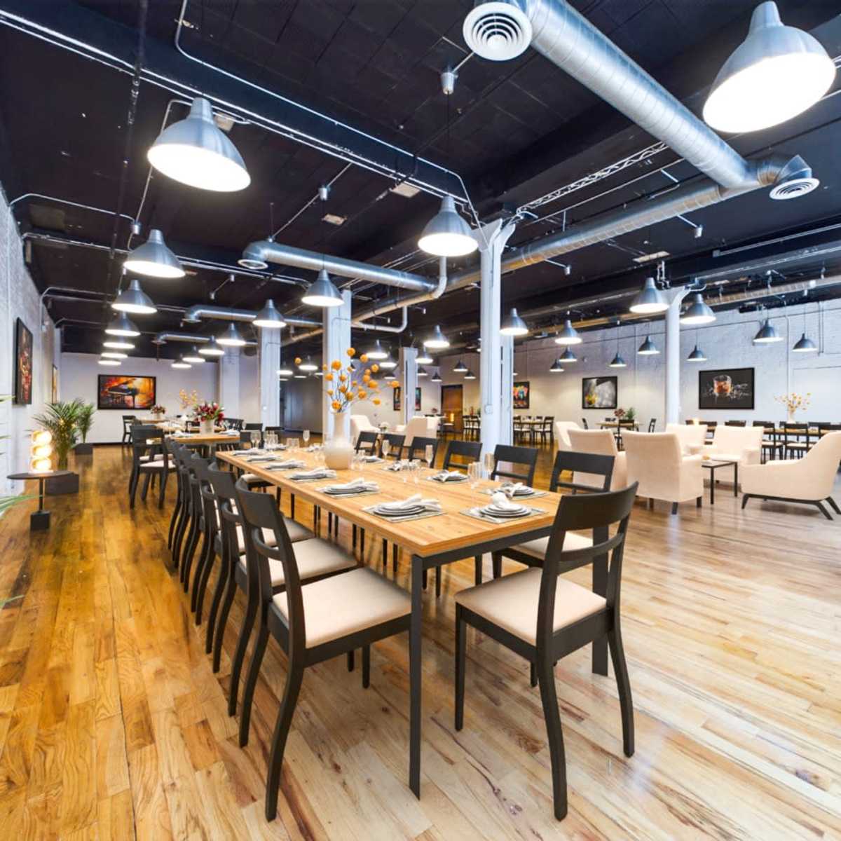 A spacious restaurant with wooden floors, featuring multiple dining tables and soft lighting, along with art on the walls.