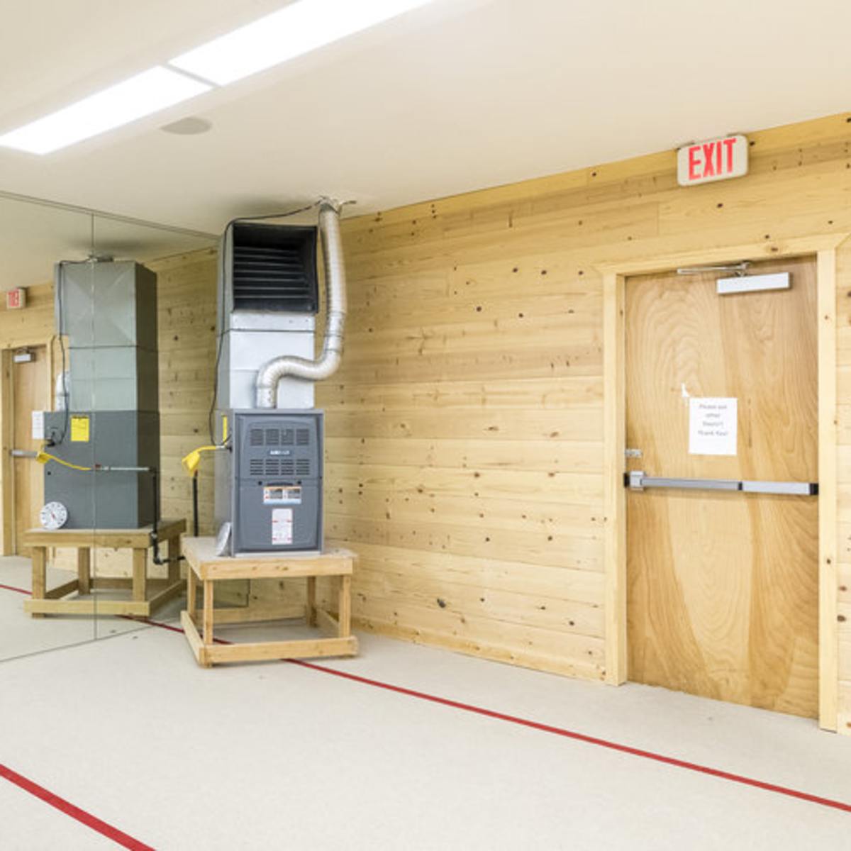 A hallway with wooden walls, a ventilation system on the left, and an exit door on the right.