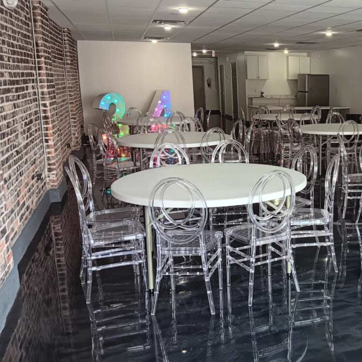 A spacious room filled with multiple round tables and clear, acrylic chairs, featuring a modern design and polished flooring.