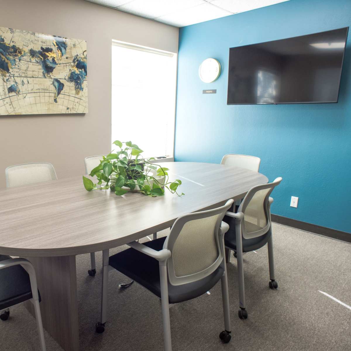 A conference room features an oval table surrounded by six chairs, with a map on the wall and a television mounted nearby.