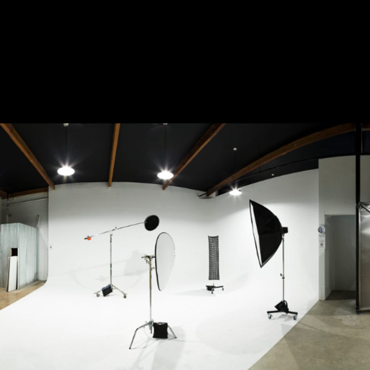 A spacious photography studio featuring a white backdrop, lighting equipment, and a rack with clothing against a stark industrial interior.
