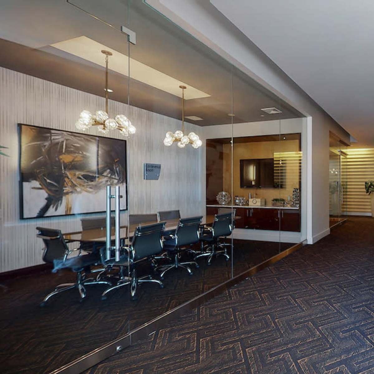 A modern office interior featuring a glass-walled conference room, a sleek desk with computers, and decorative lighting.
