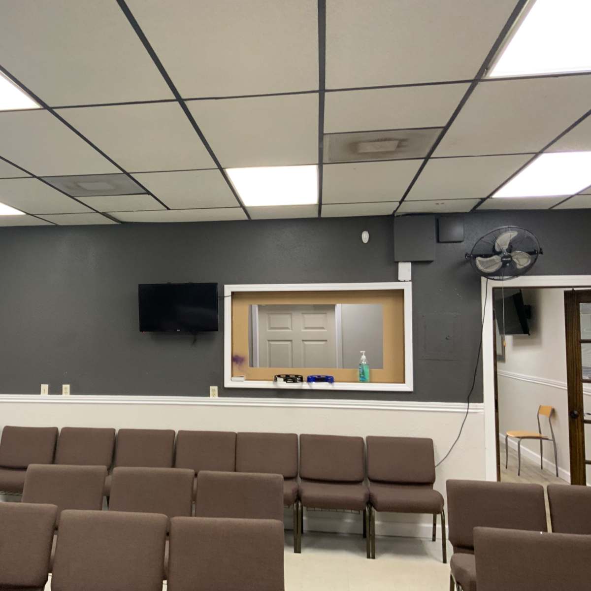 A seating area in a room with gray walls, a television mounted on the wall, and a small window to another room.