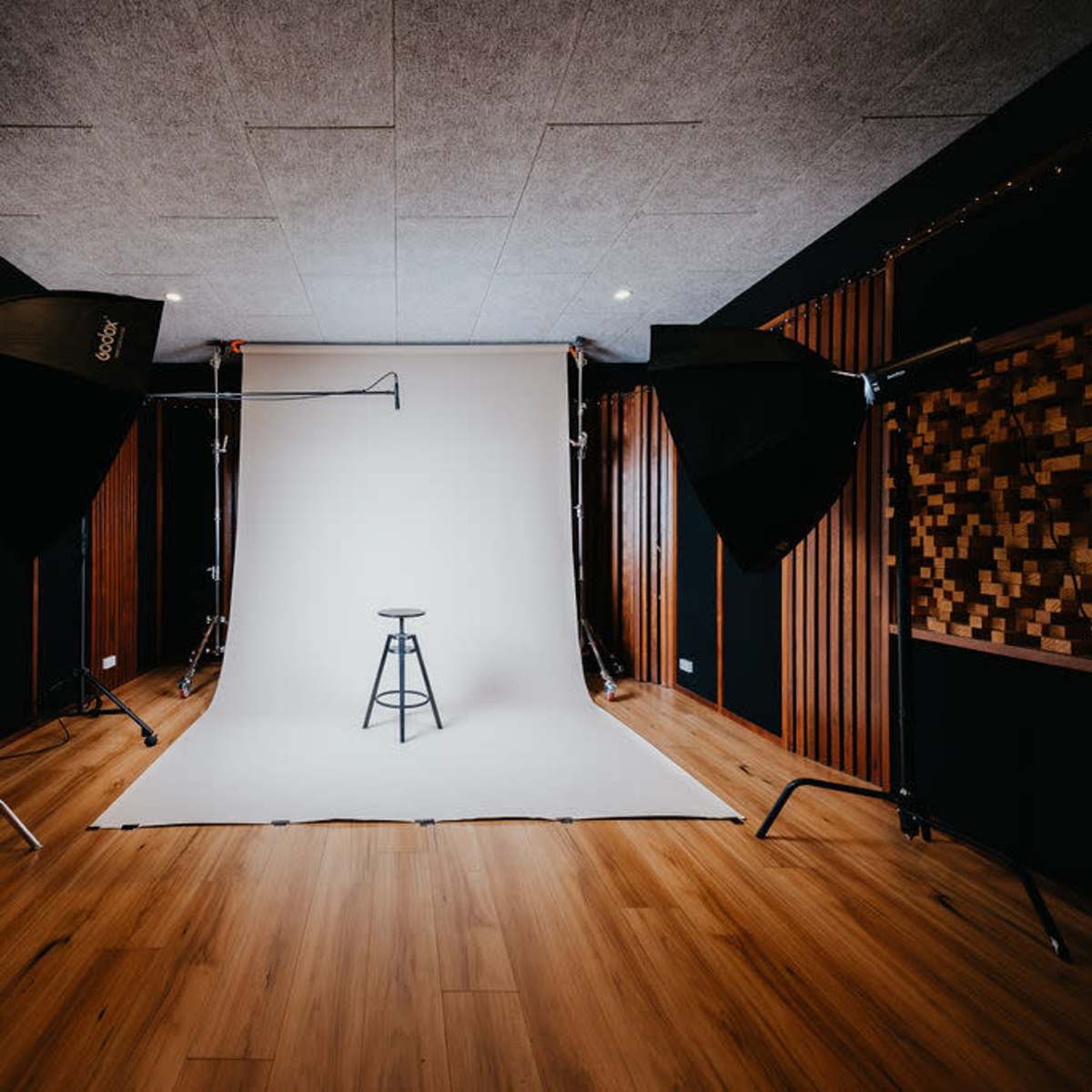 A photo studio with a plain backdrop, a stool in the center, and two large softbox lights positioned on either side.