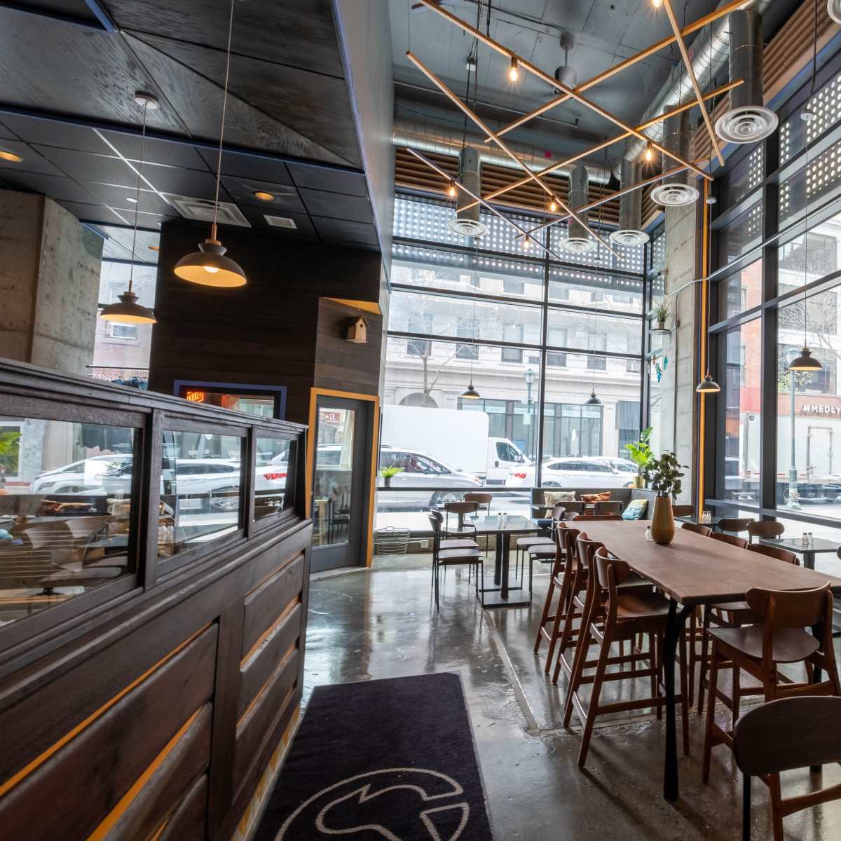 A modern café features large windows, wooden tables, and a minimalist interior design.