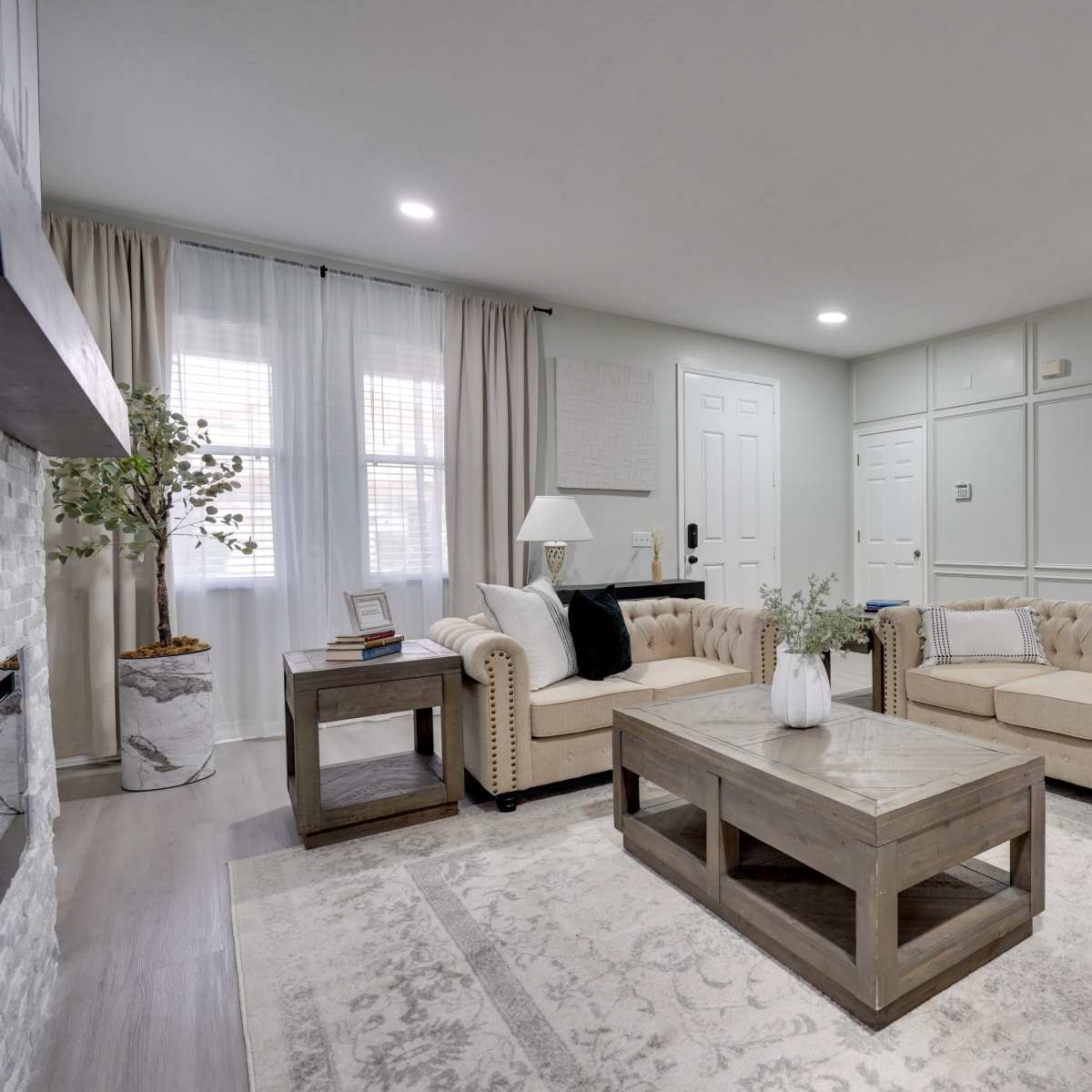 A living room featuring two beige tufted sofas, a wooden coffee table, and gray walls with decorative paneling.