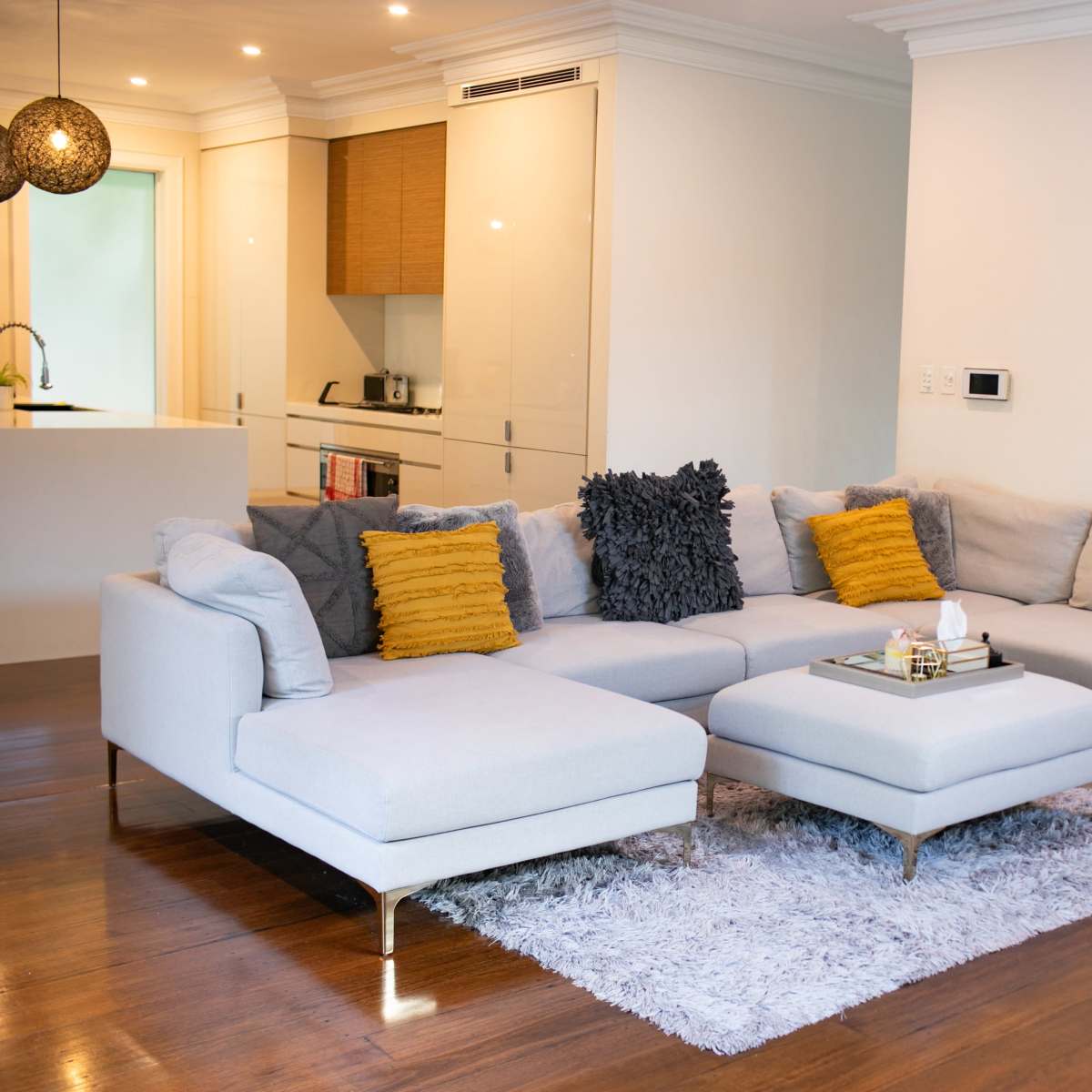 A modern living room with a light gray sectional sofa, a plush area rug, and two colorful paintings on the wall.