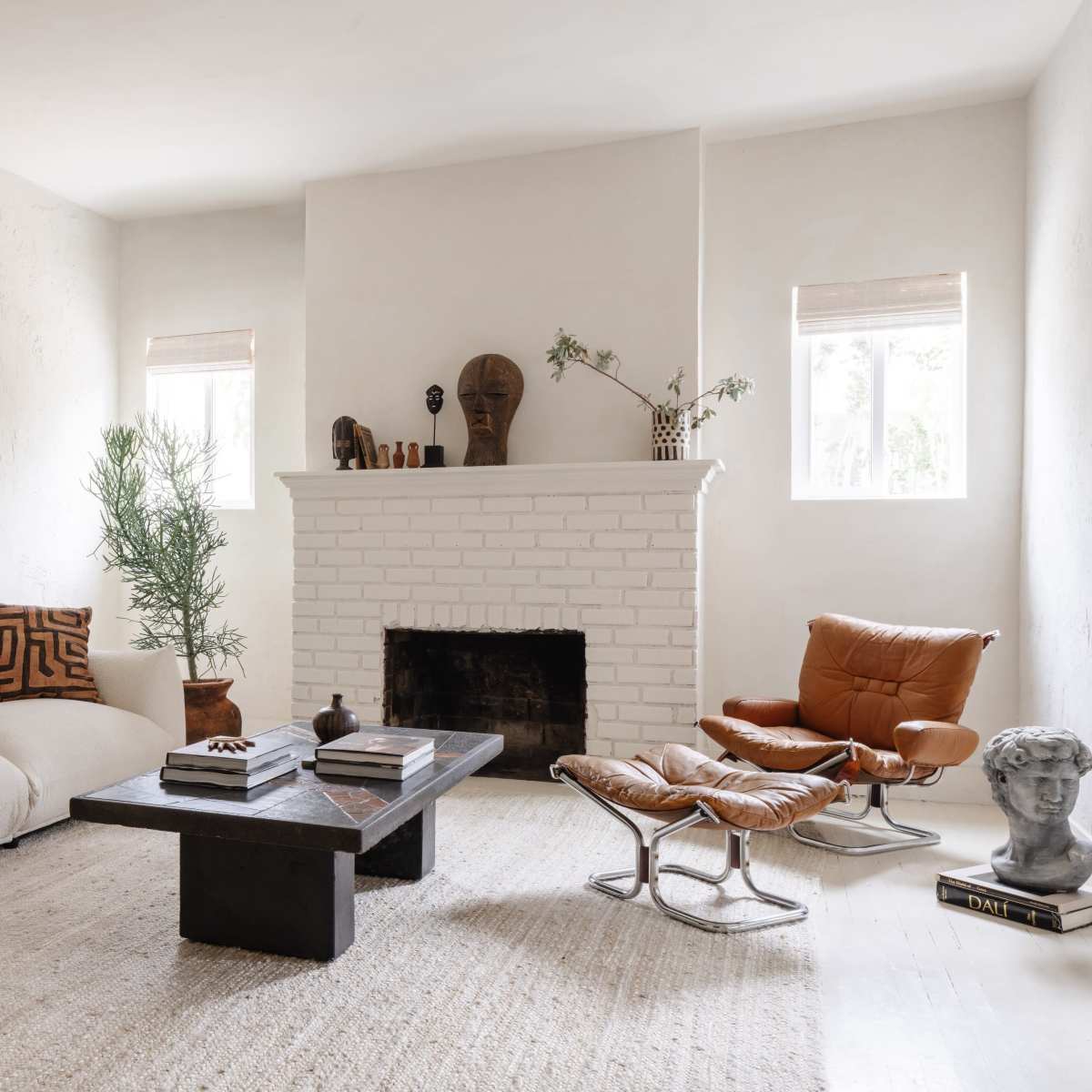A minimalist living room with a white sofa, a dark wooden coffee table, and a fireplace with decorative objects on the mantel.