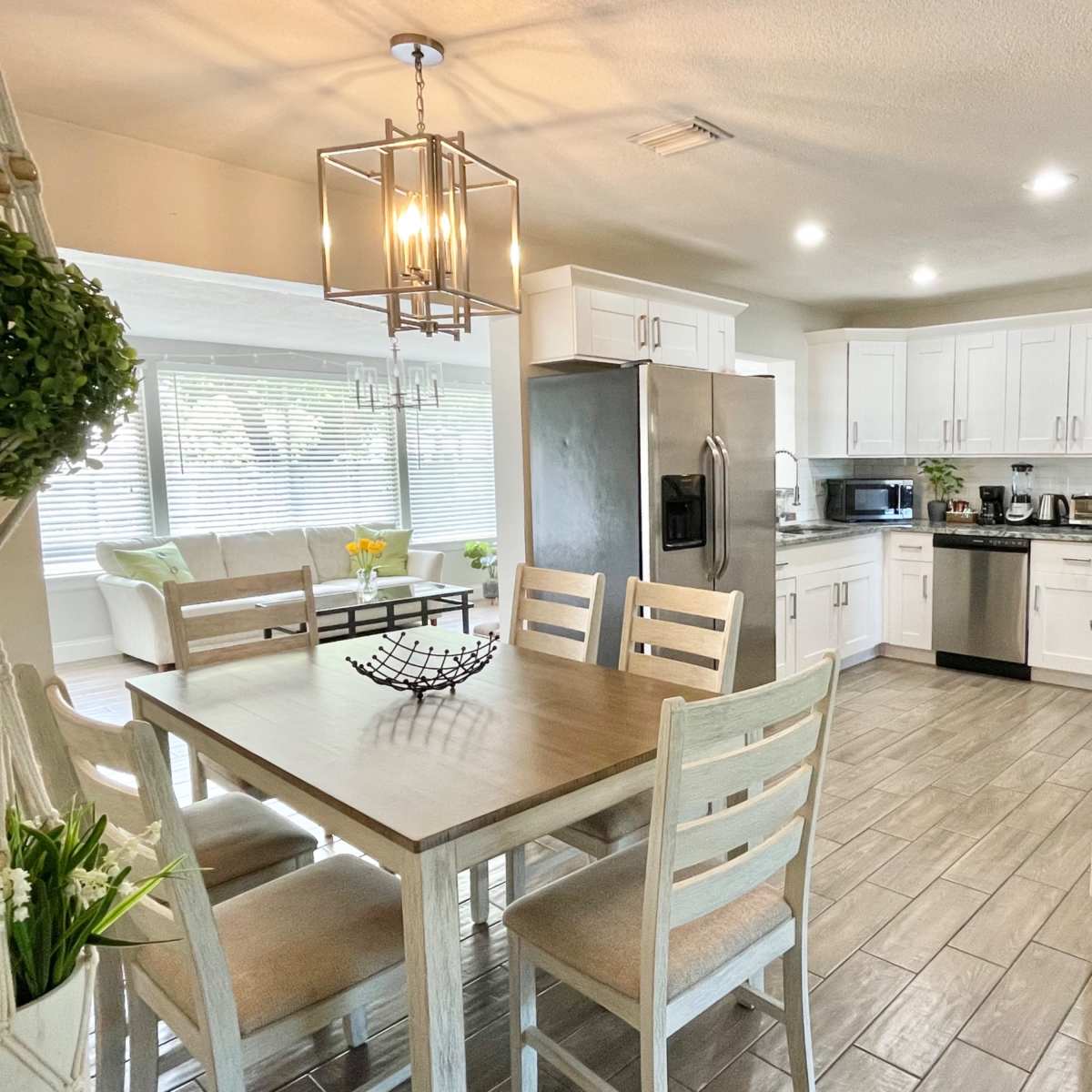 A modern kitchen with white cabinets, stainless steel appliances, and a dining table set for four, illuminated by a hanging light fixture.