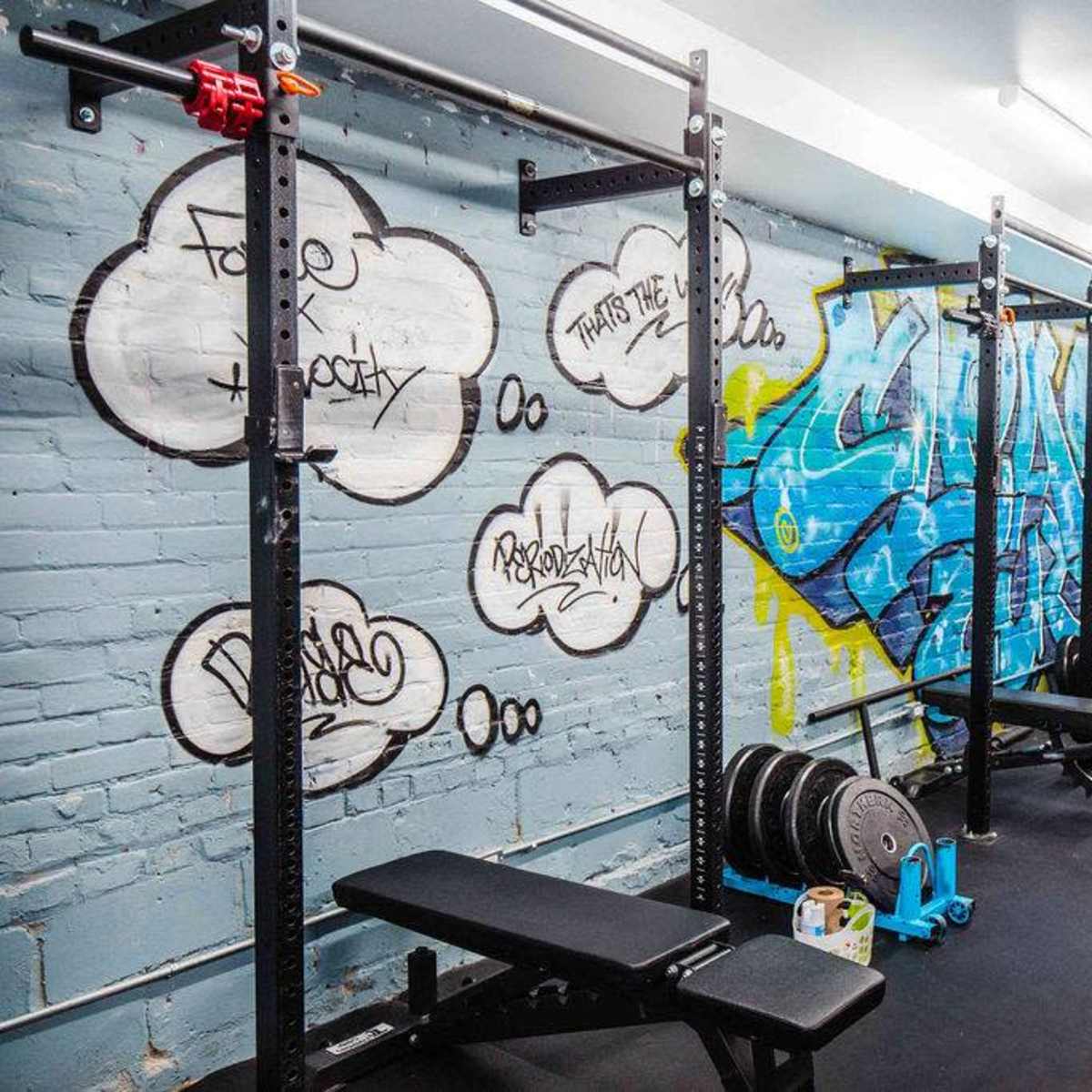 A gym interior with weightlifting equipment and colorful graffiti on the walls.