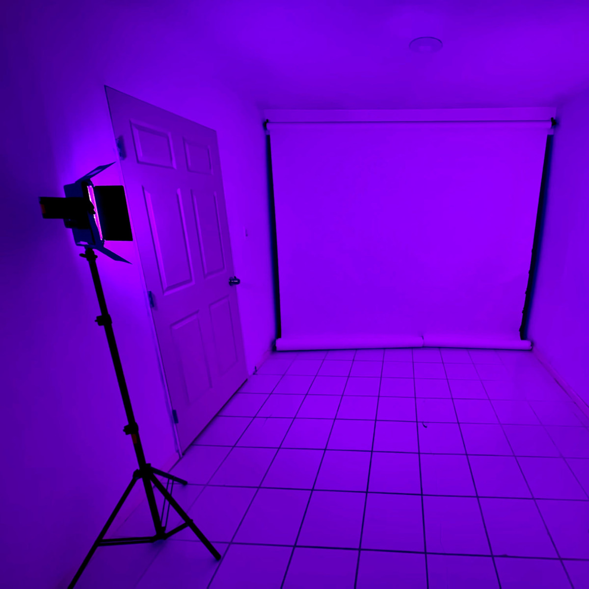 A sparsely furnished room with two lighting setups positioned on either side of a blank white backdrop.