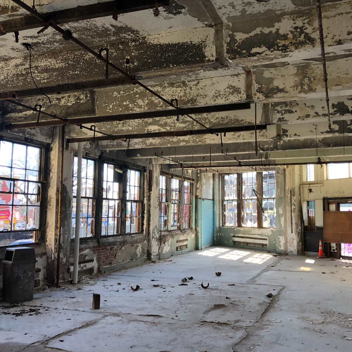 An empty, dilapidated room with peeling paint and large windows that allow natural light to enter.