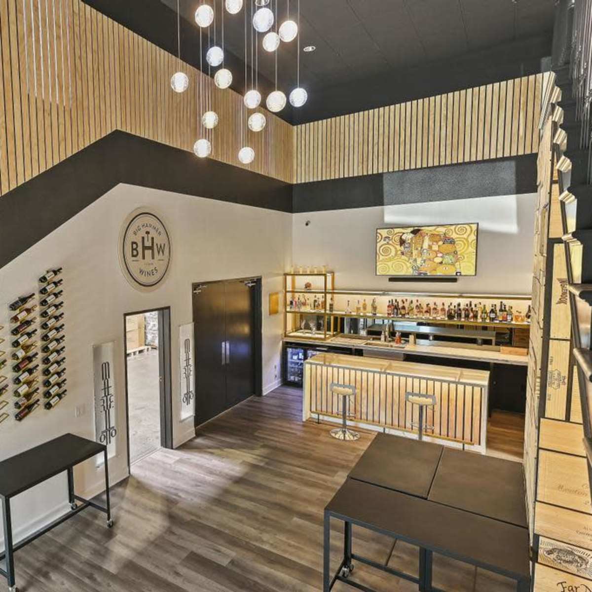 A modern interior of a bar or lounge with wooden paneling, a staircase, and a well-stocked bar counter at the back.