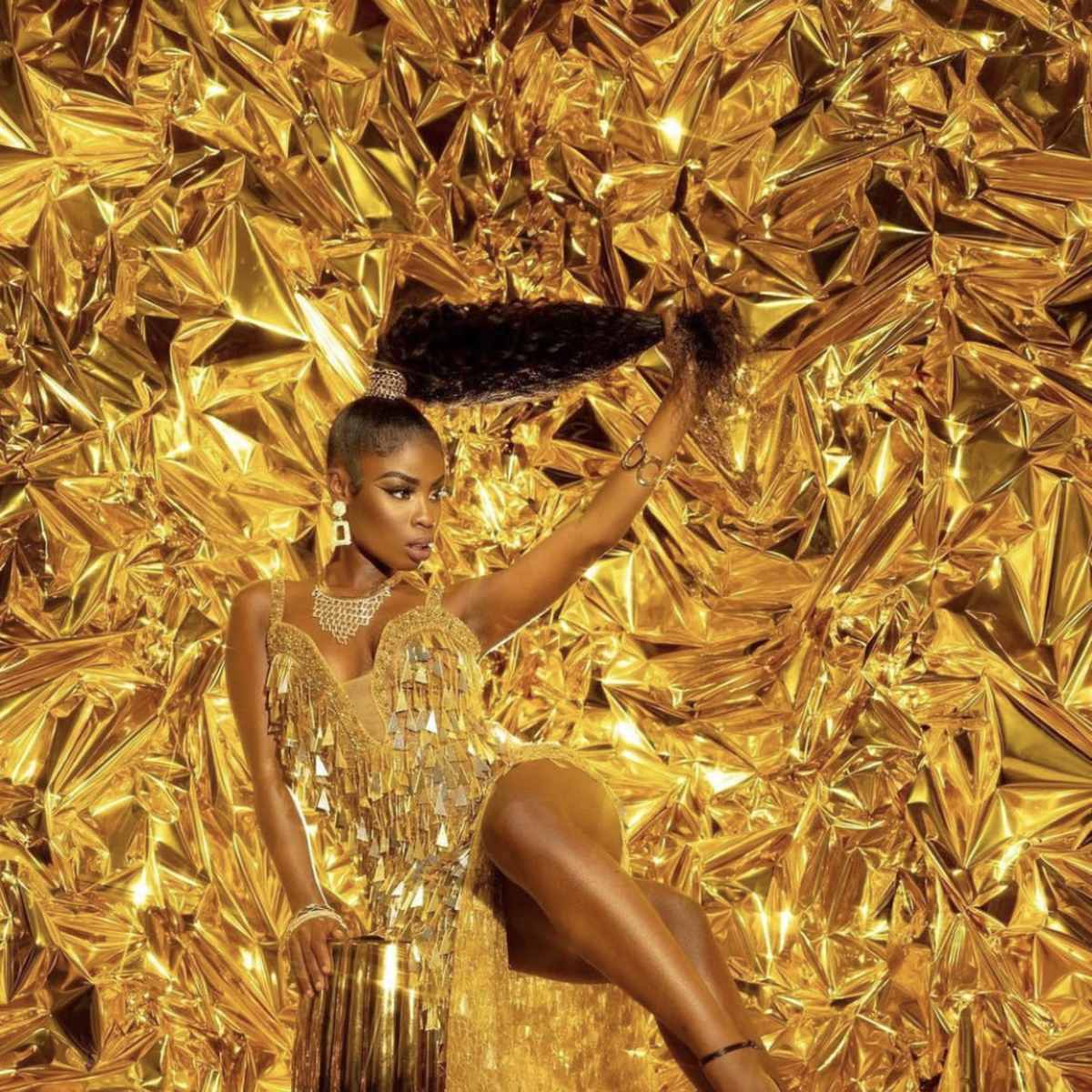 A woman poses in a gold fringed outfit against a backdrop of crumpled gold foil.