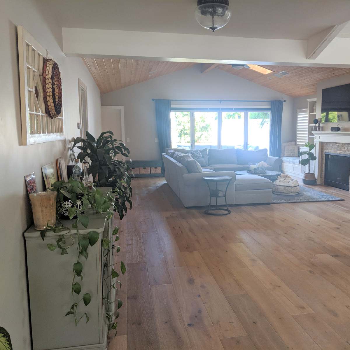 The room features a spacious living area with a large sectional sofa, a coffee table, and a dining area, all illuminated by natural light from large windows.