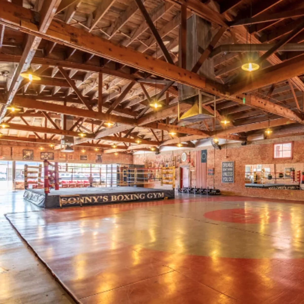 An interior view of a boxing gym with a large training area, boxing ring, and various equipment along the walls.