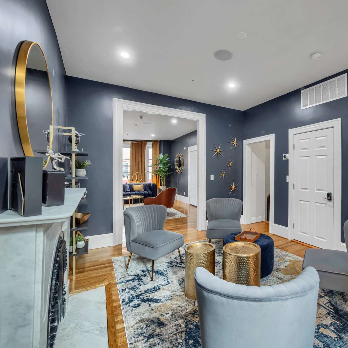 A modern living room featuring a blue wall, a marble fireplace, four chairs arranged around metallic accent tables, and a decorative rug.