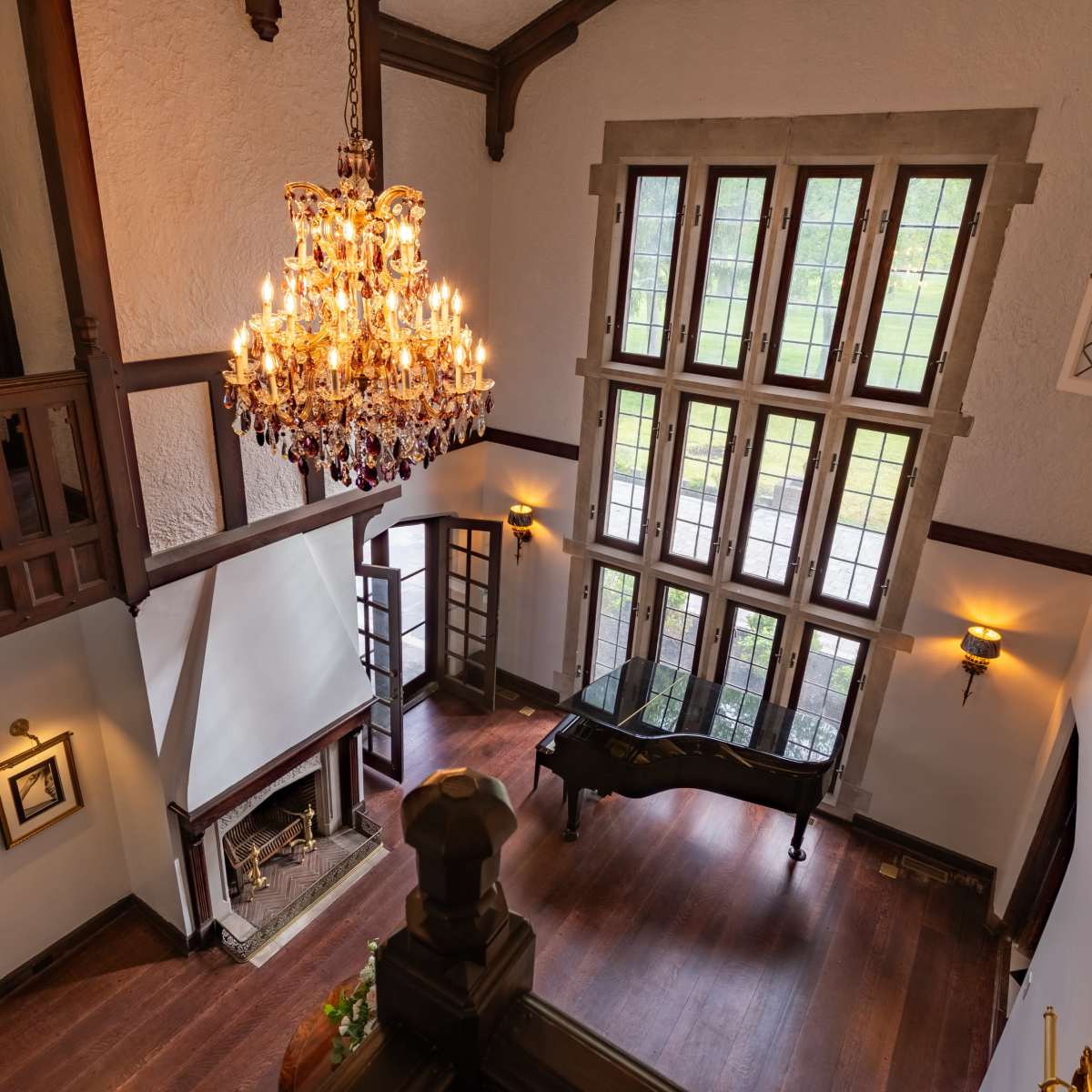 A spacious interior with a high ceiling, featuring a large chandelier, a grand piano near the windows, and a fireplace.