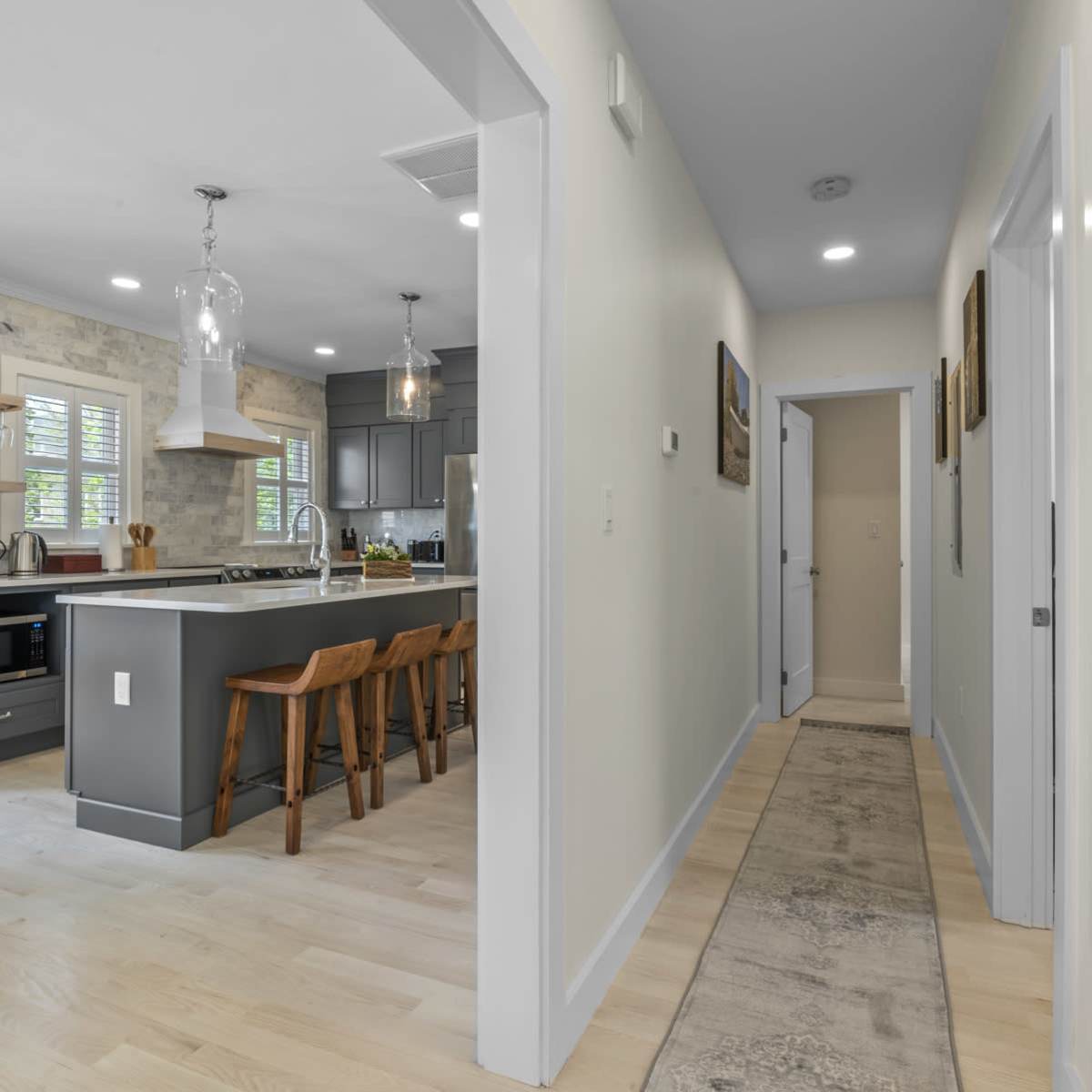 A hallway leads to a kitchen with a central island and seating, featuring modern cabinets and appliances.