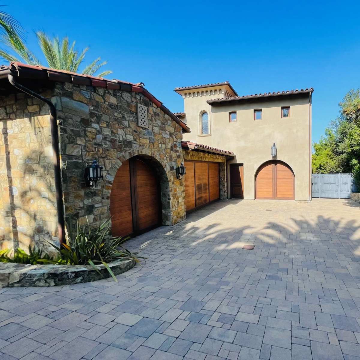 An exterior view of a stone and stucco house with a paved driveway and two wooden garage doors.