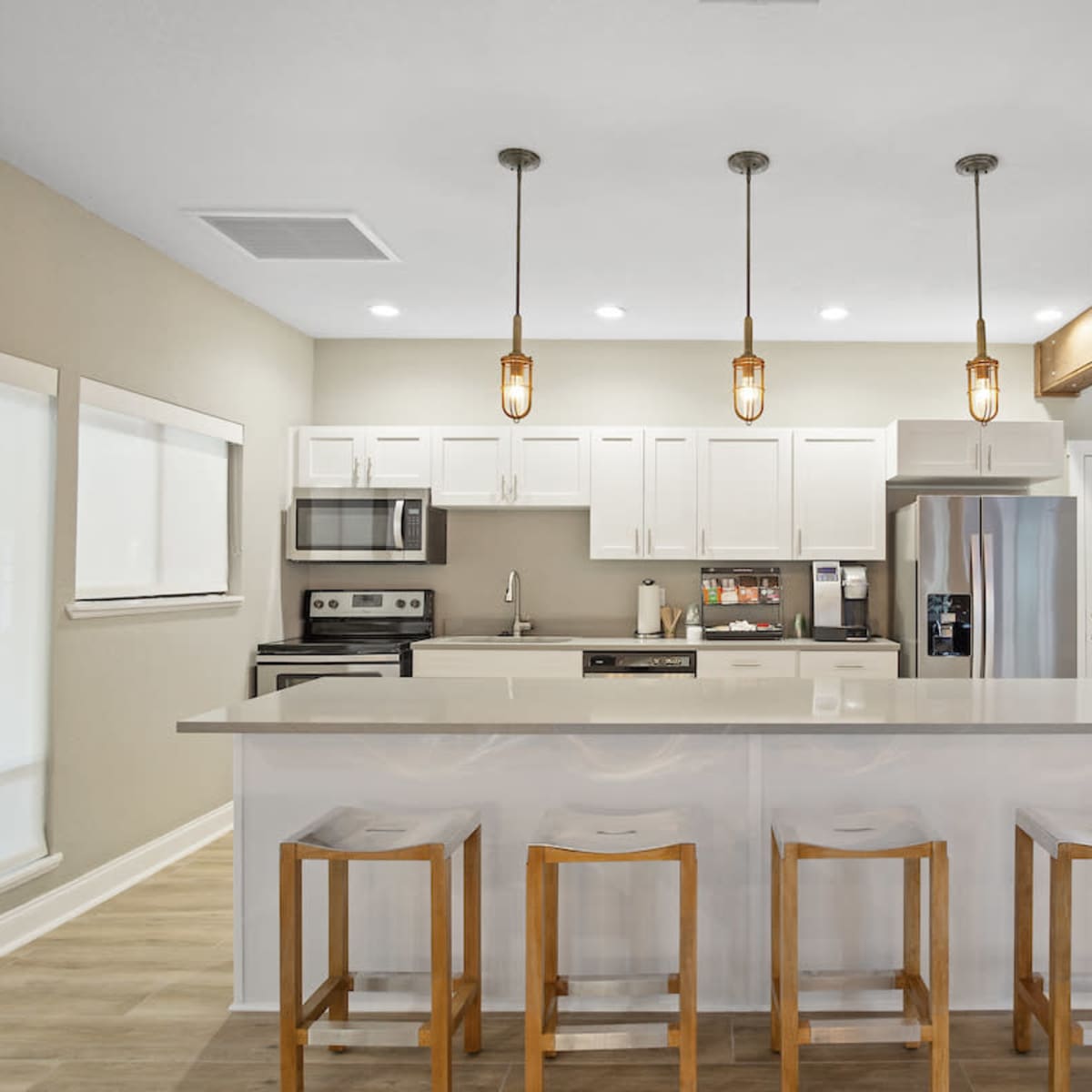 A modern kitchen features white cabinetry, stainless steel appliances, and a central island with four wooden barstools.