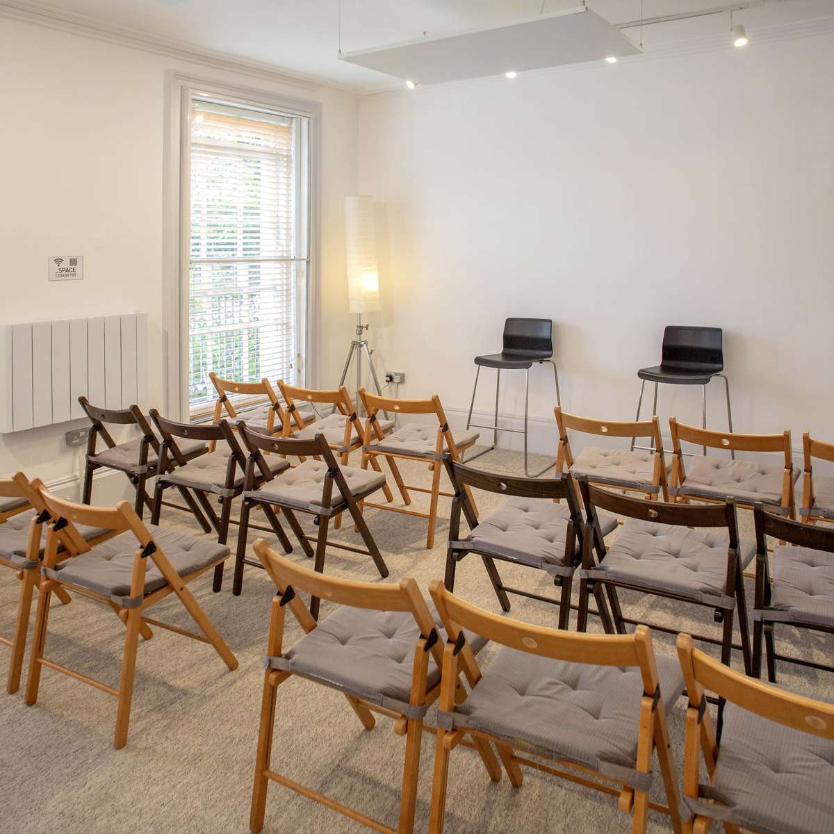 A room with rows of wooden folding chairs arranged facing two black chairs at the front.