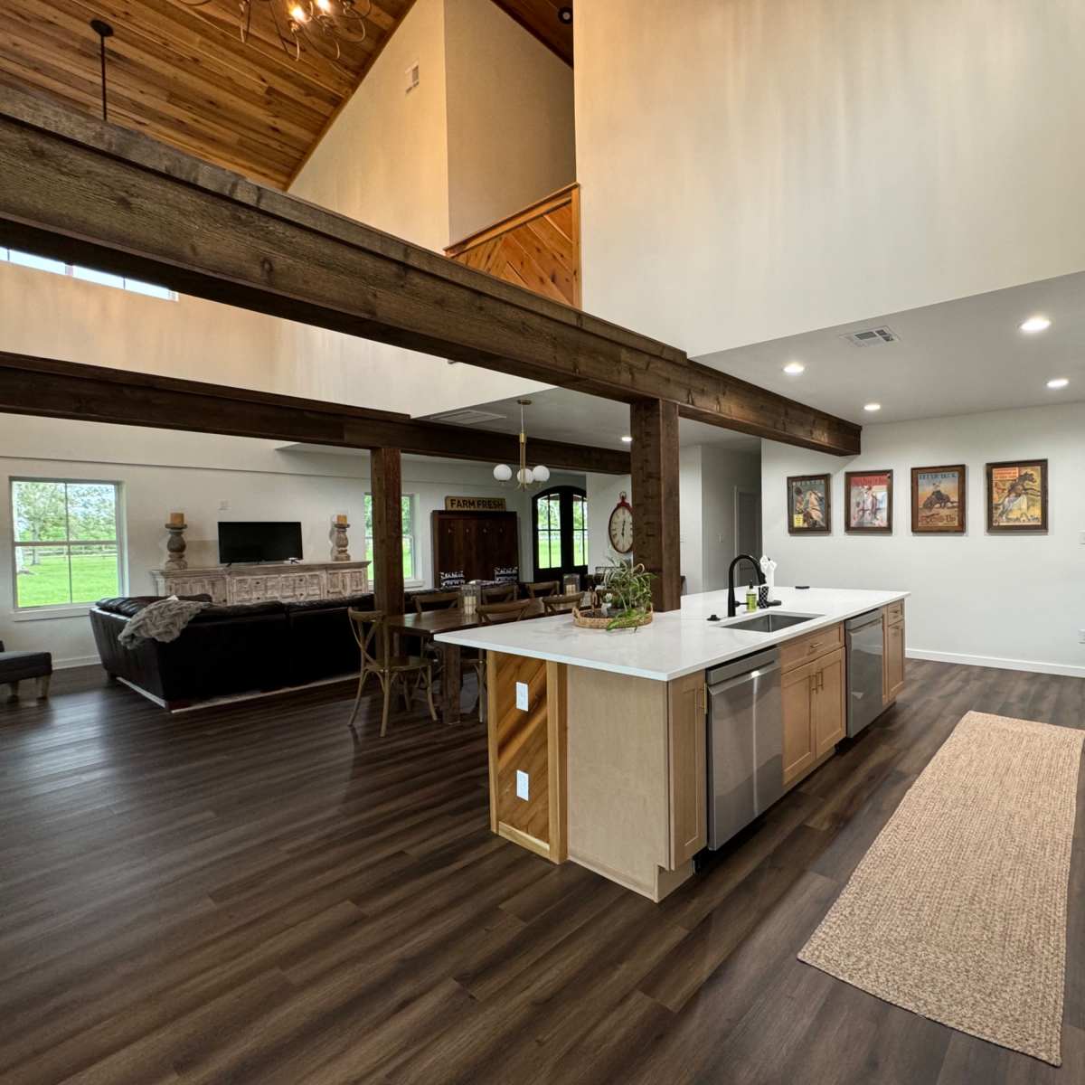 A modern kitchen with an island, stainless steel appliances, and a view of a living area featuring wooden beams and large windows.