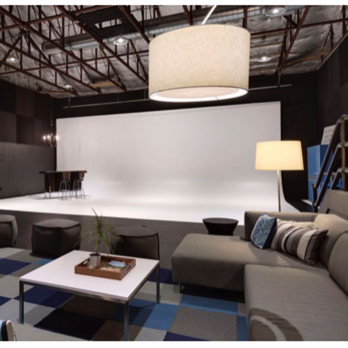 A spacious photography studio features a lounge area with couches, coffee tables, and aesthetic lighting, adjacent to a bright white backdrop.