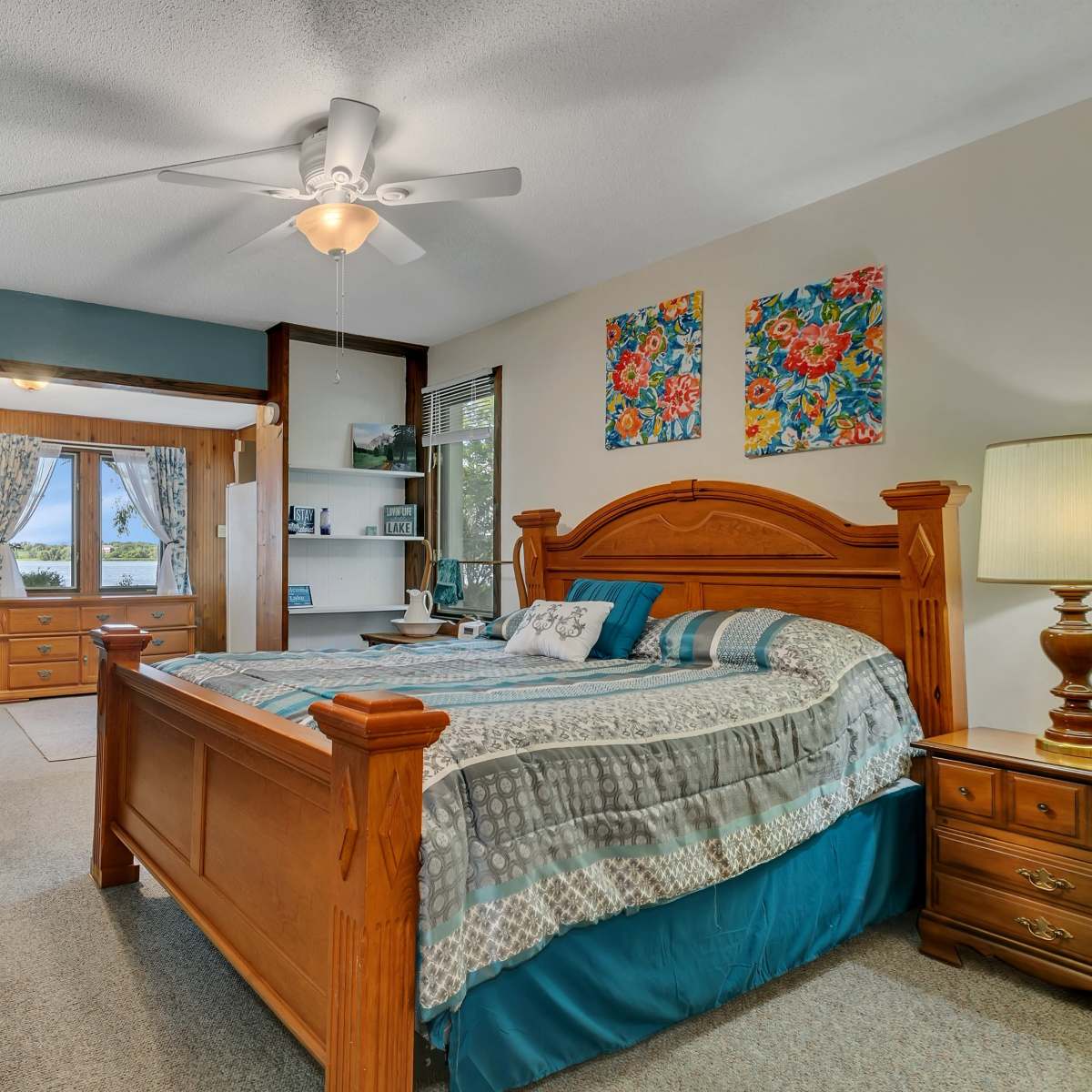 A well-furnished bedroom featuring a wooden bed with a patterned comforter, two nightstands, and a doorway leading to another room.