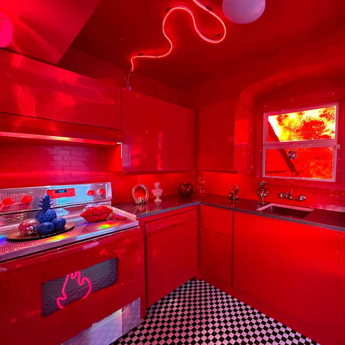 The kitchen features red walls, cabinets, and appliances, with a checkerboard floor and various decorative items arranged on the countertops.